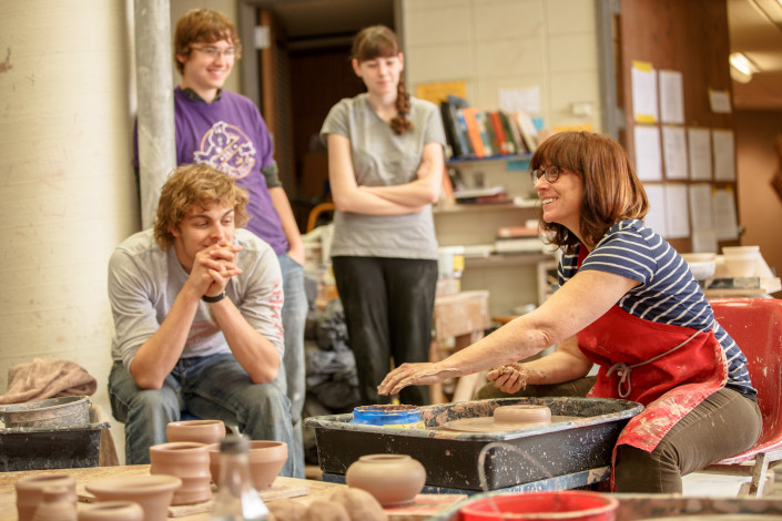 Prof. Kimberly Greene demonstrates to students how to throw clay in a pottery class.