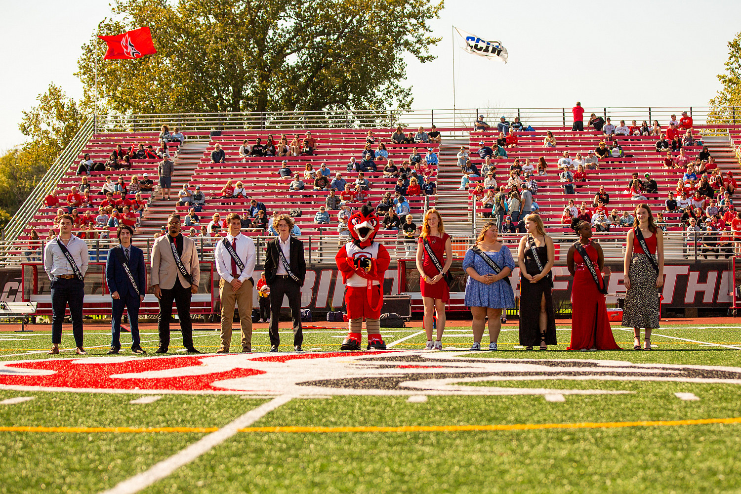 Students dressed in dresses and suits wearing crowns on the football field.