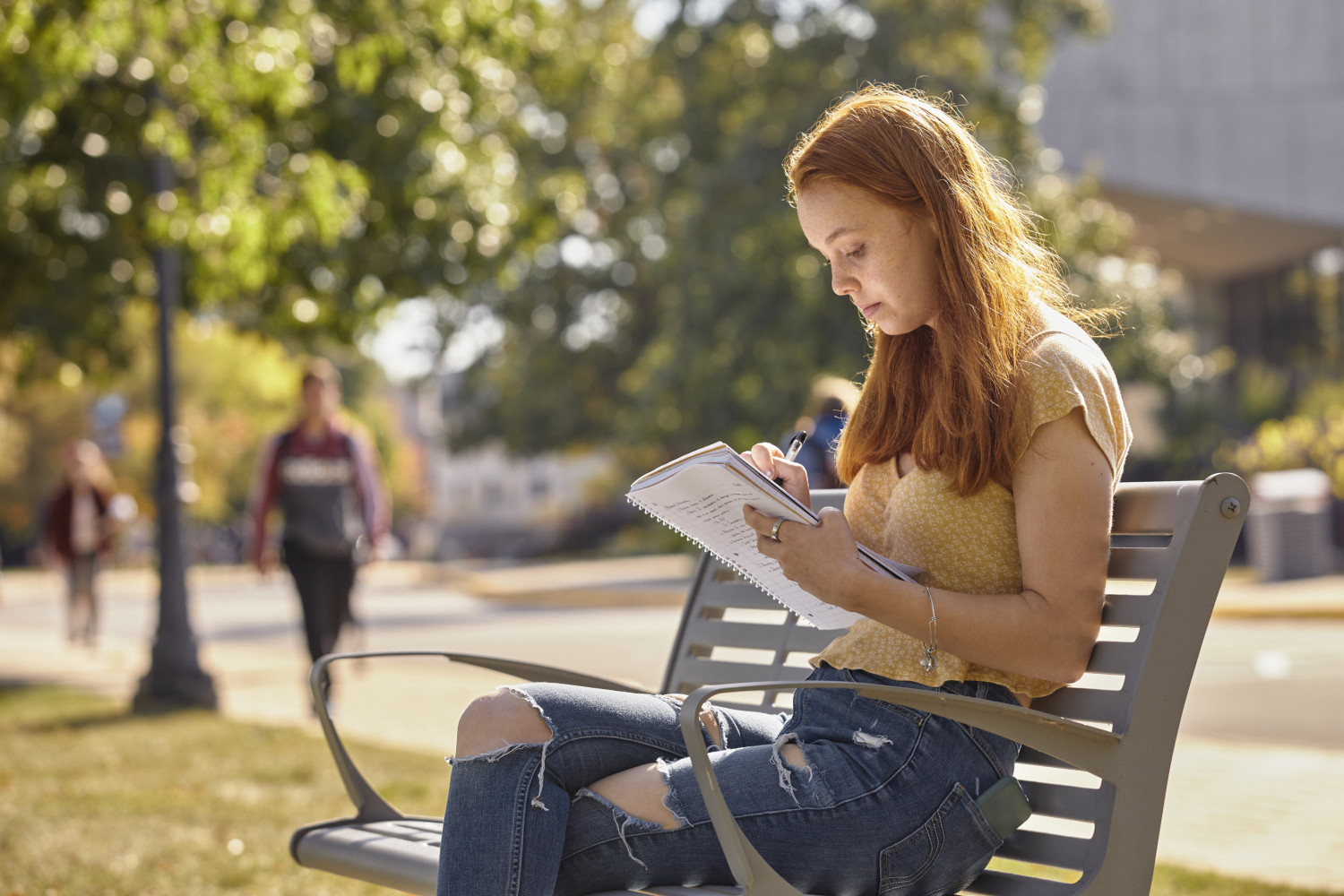 A Carthage College student reads on a bench along Campus Drive.