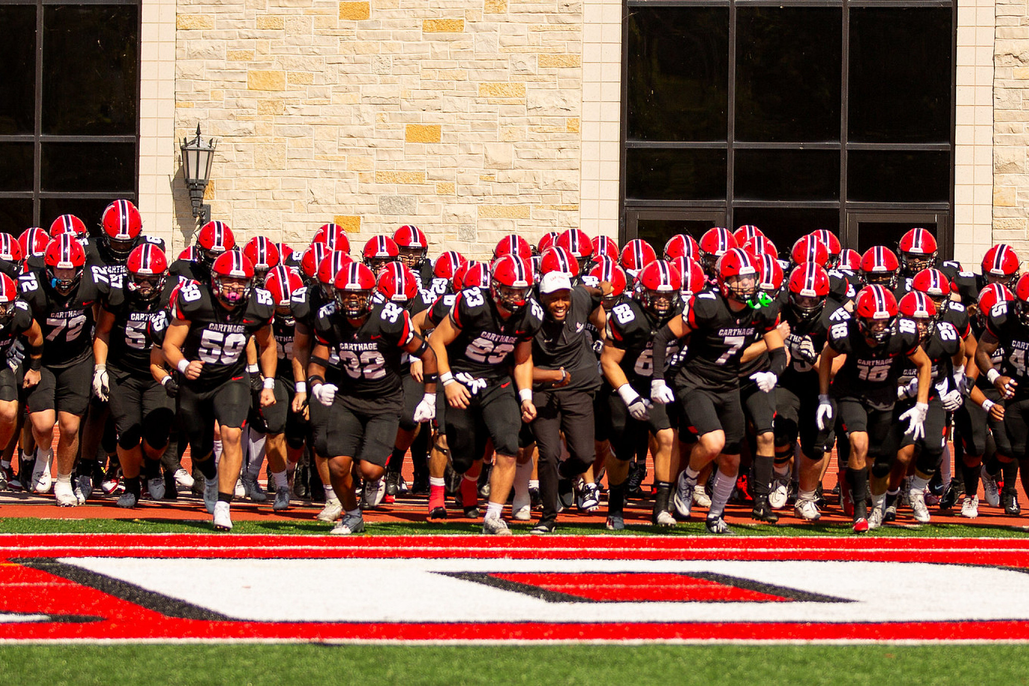 The Carthage football team dressed in their uniforms running onto the football field.