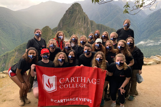 Group study tour picture holding Carthage flag in front of Machu Picchu