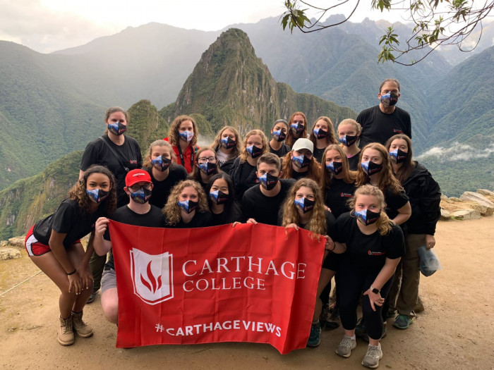Group study tour picture holding Carthage flag in front of Machu Picchu