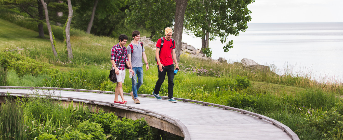 Three Carthage students walk along a lakefront pathway toward the outdoor classroom.