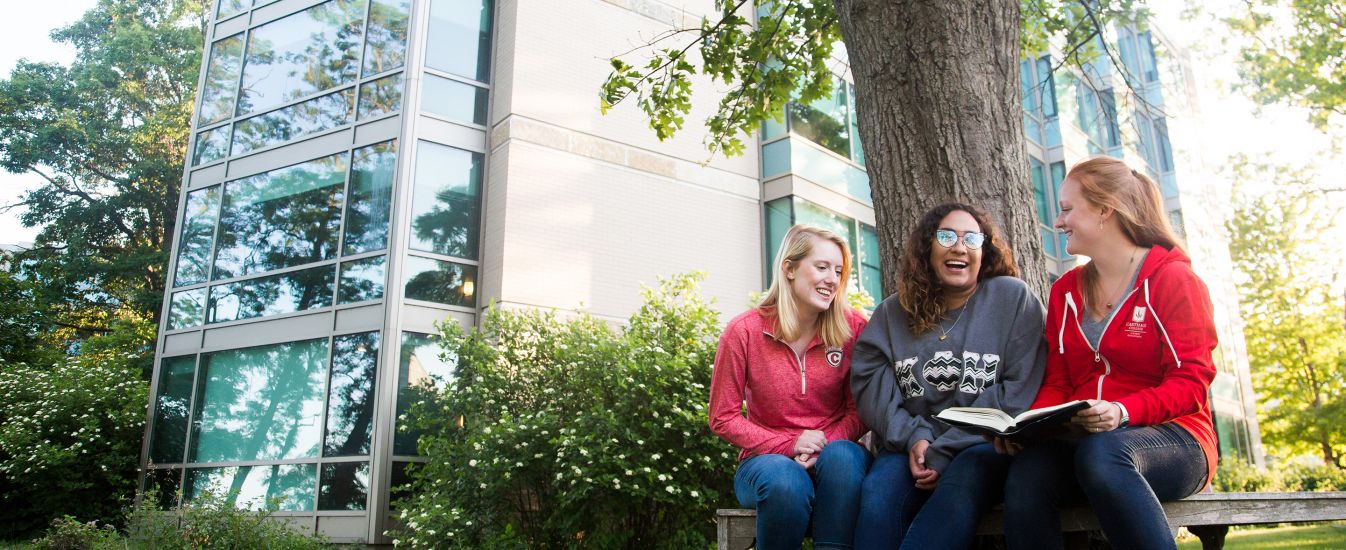 Three students laugh on a bench outside The Oaks.