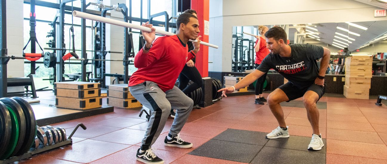 A student practices squatting with assistance from an instructor. 