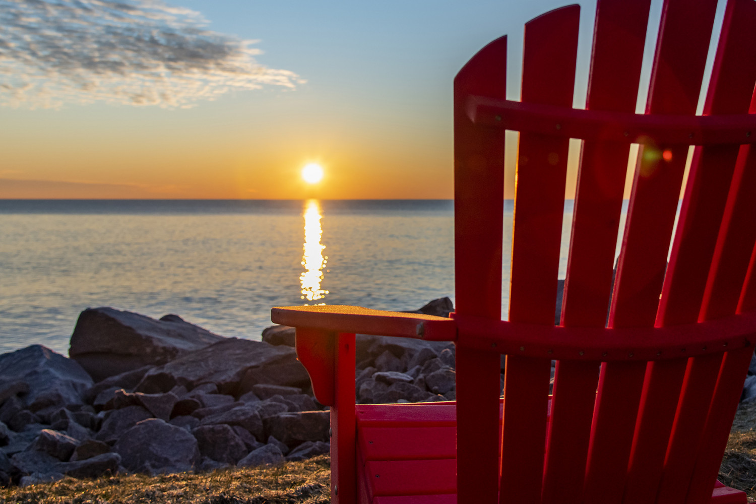 A red Adirondack chair facing the lake at sunrise.