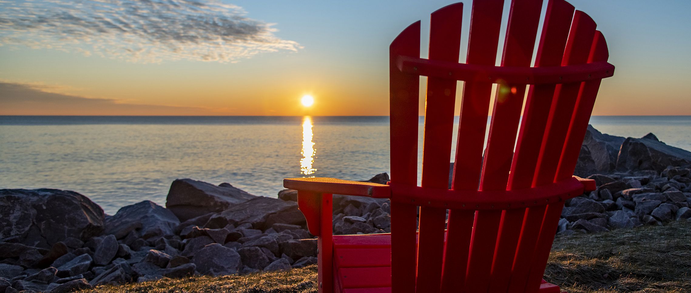 A red Adirondack chair facing the lake at sunrise.