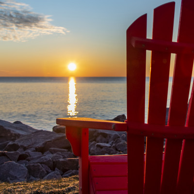 A red Adirondack chair facing the lake at sunrise.