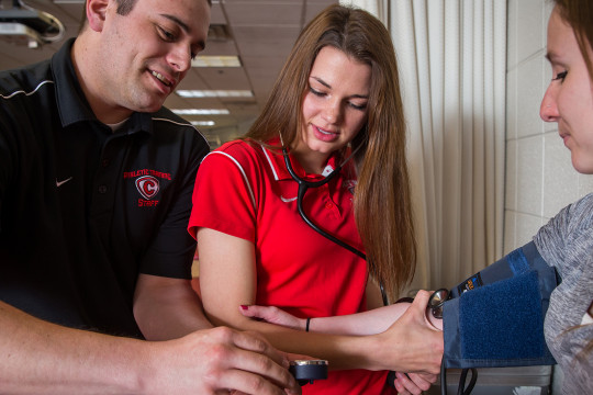 A faculty member guides an allied health science student through a health check.