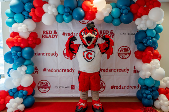 Ember the mascot posing in front of the Red and Ready backdrop.