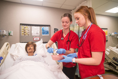 Carthage students majoring in nursing work with a human simulator mannequin.