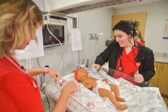 Carthage students majoring in nursing work with a baby human simulator mannequin.
